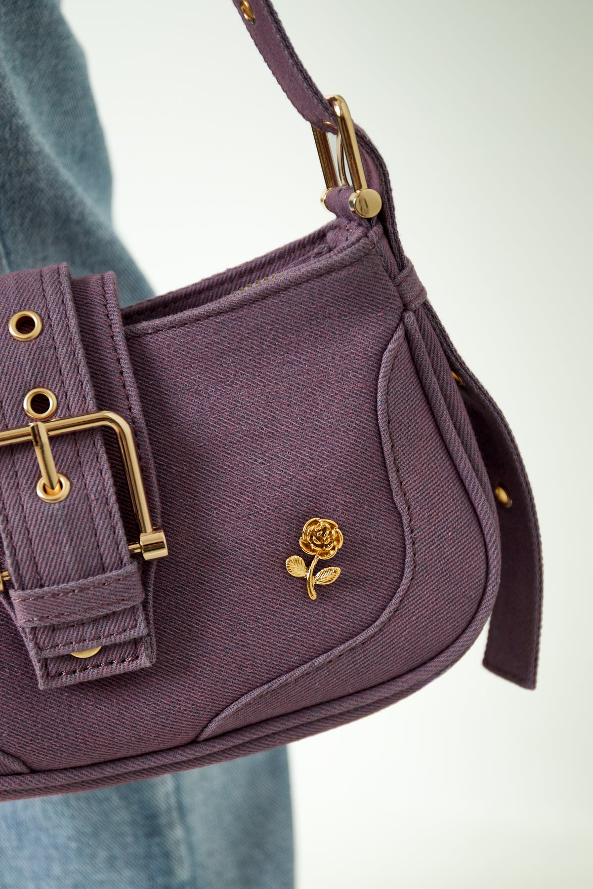 Gold rose brooch pinned on a purple handbag strap with denim jeans in background, showcasing style use