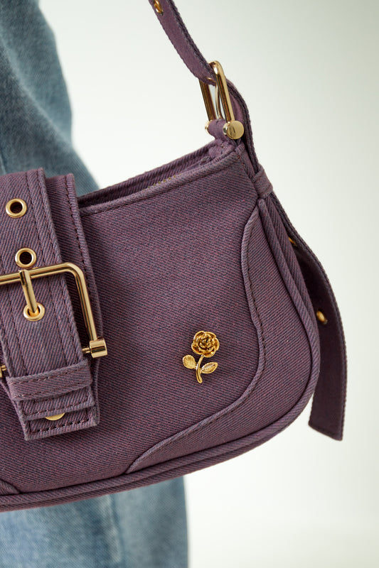 Gold rose brooch pinned on a purple handbag strap with denim jeans in background, showcasing style use