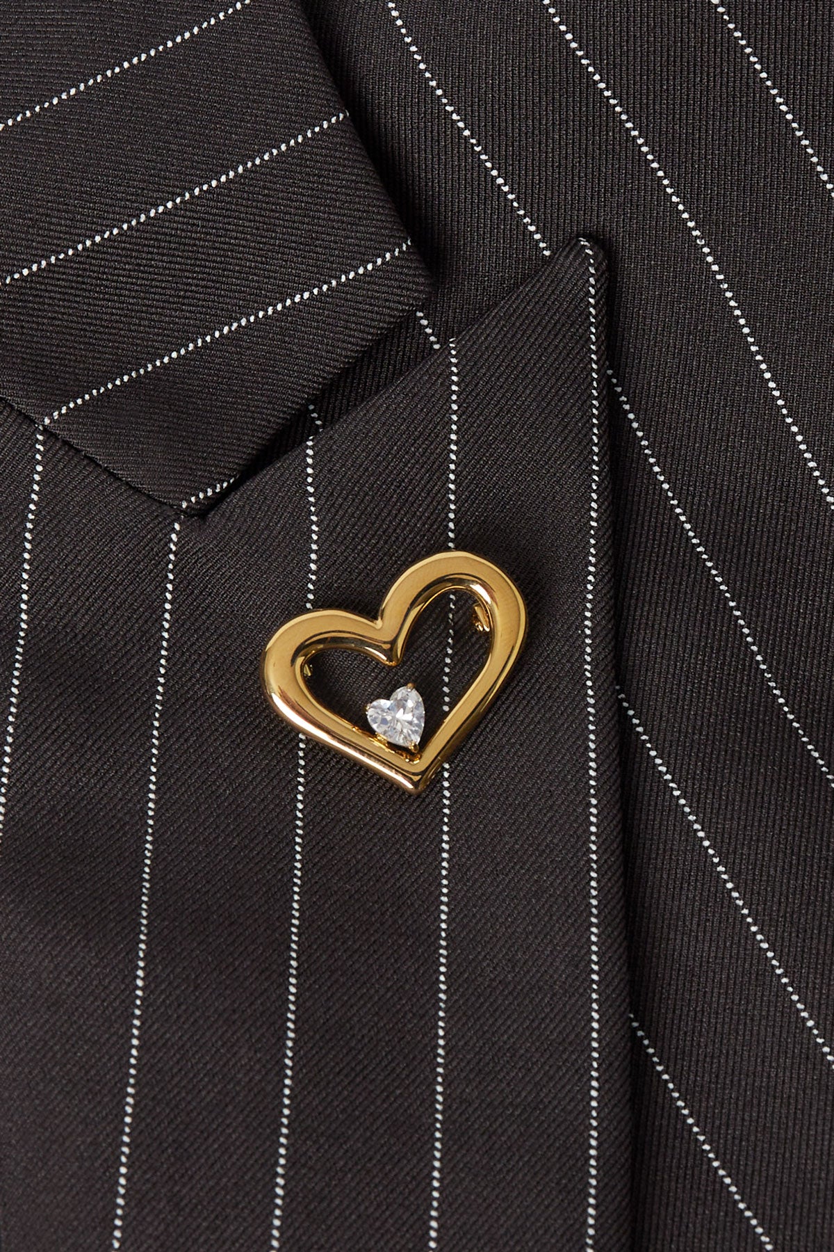 Gold heart-shaped brooch pinned on black pinstripe suit lapel close-up