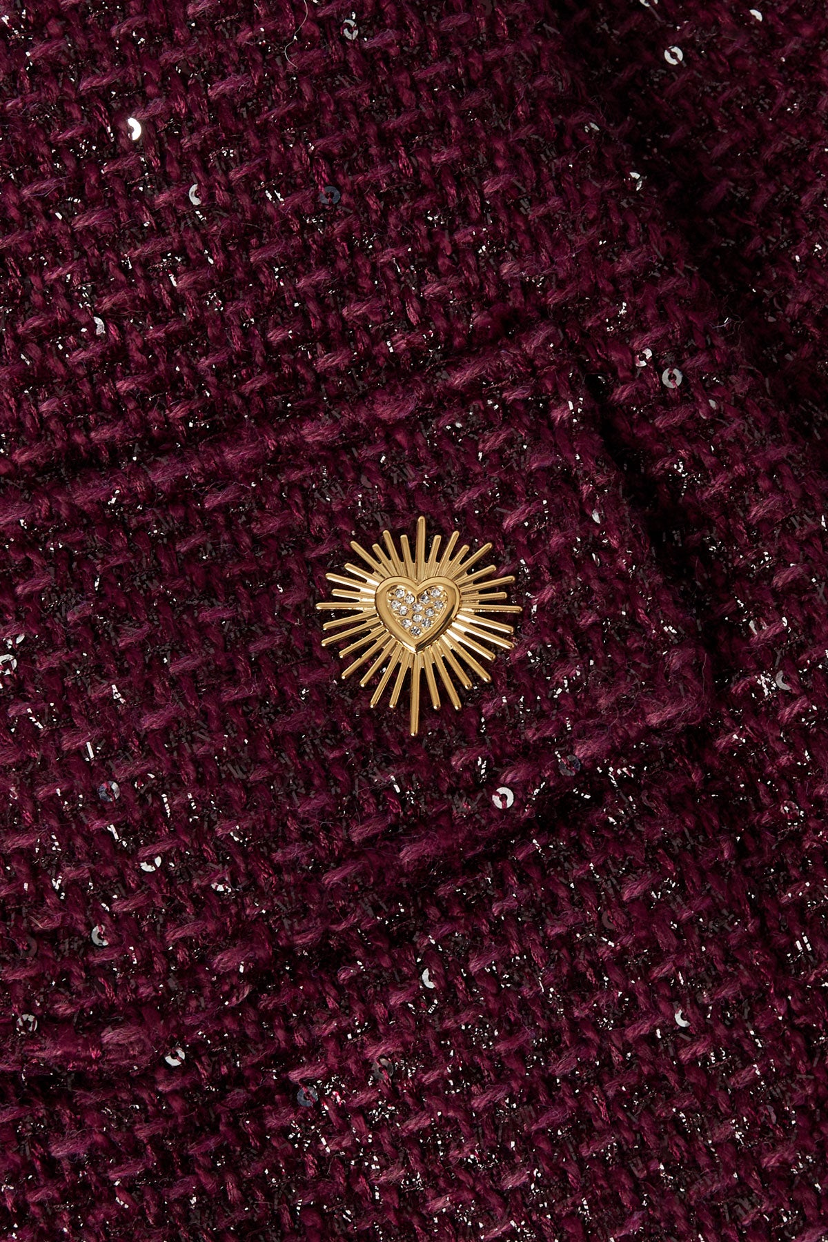 Close-up of the gold sunburst heart brooch pinned on textured dark plum tweed jacket