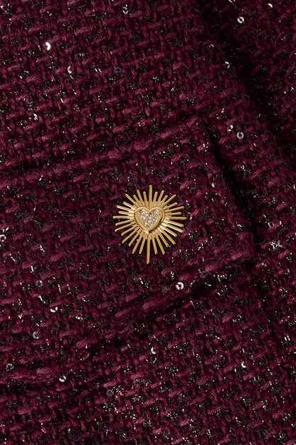 Close-up of the gold sunburst heart brooch pinned on textured dark plum tweed jacket