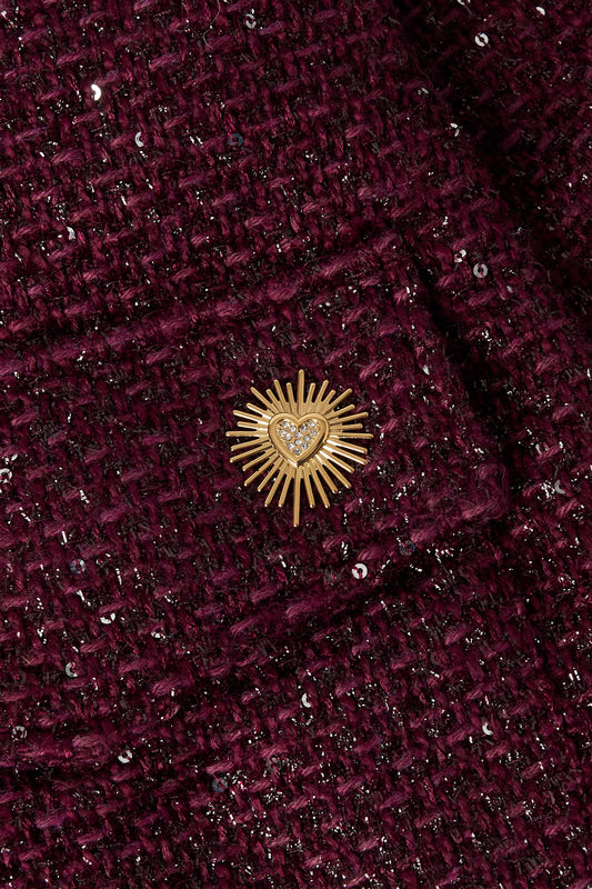 Close-up of the gold sunburst heart brooch pinned on textured dark plum tweed jacket