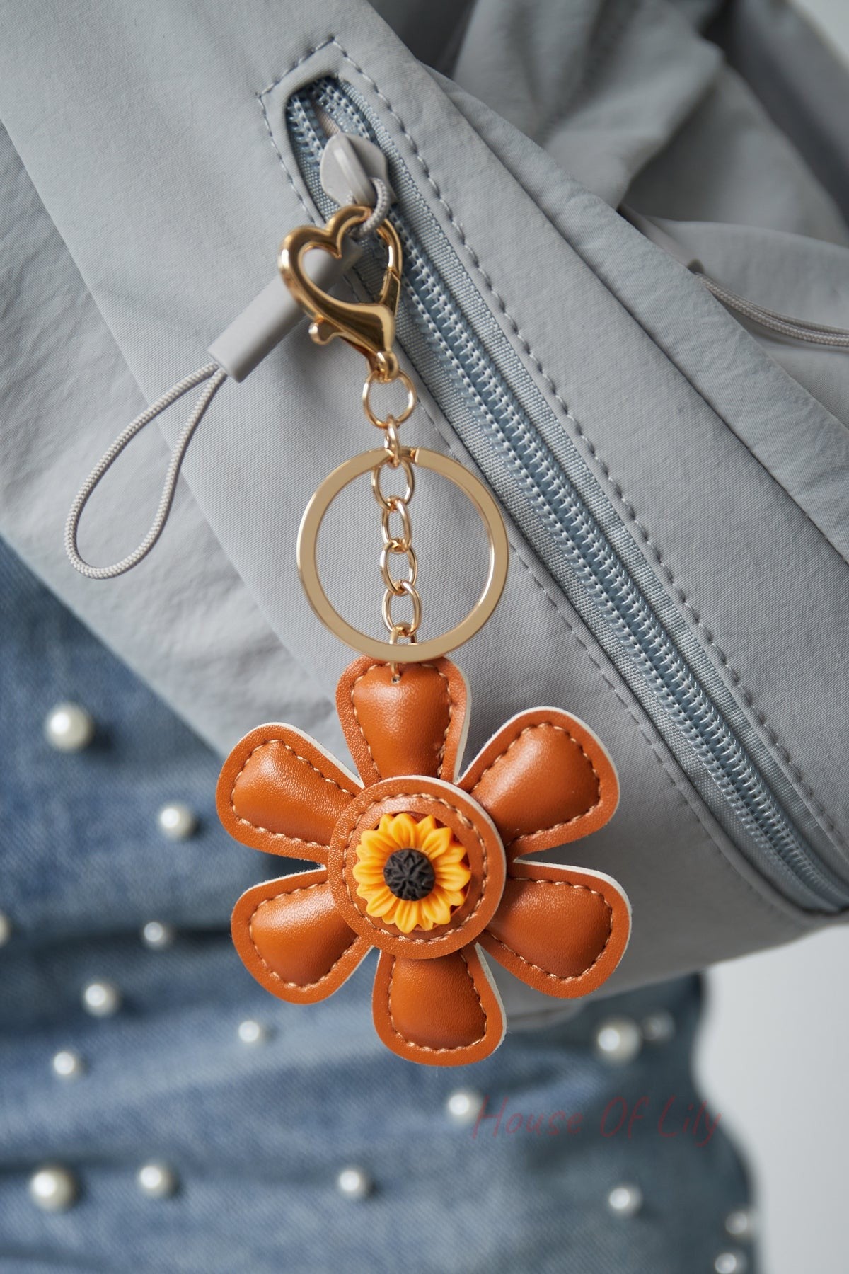 Brown faux leather floral keychain attached to a gray jacket zipper with gold heart clasp