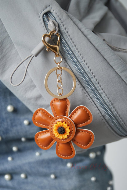 Brown faux leather floral keychain attached to a gray jacket zipper with gold heart clasp