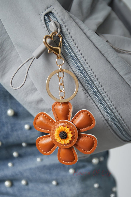 Brown faux leather floral keychain attached to a gray jacket zipper with gold heart clasp