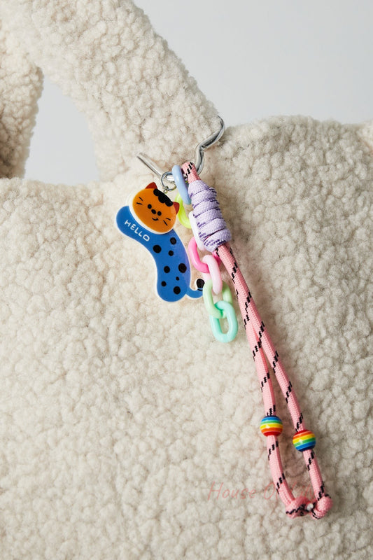 Pink cord bag charm clipped on soft cream textured fabric bag, featuring an orange cat acrylic charm with blue and pink plastic links and rainbow beads