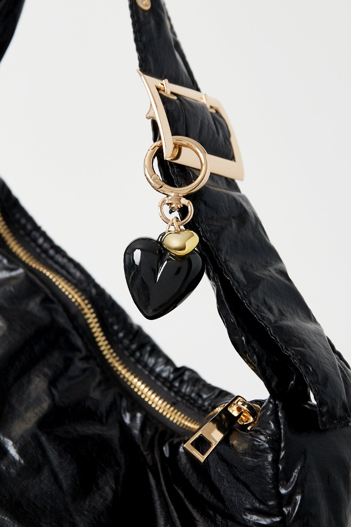 Black heart pendant keychain clipped to black bag strap with gold zipper and buckle details