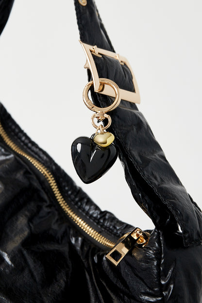 Black heart pendant keychain clipped to black bag strap with gold zipper and buckle details