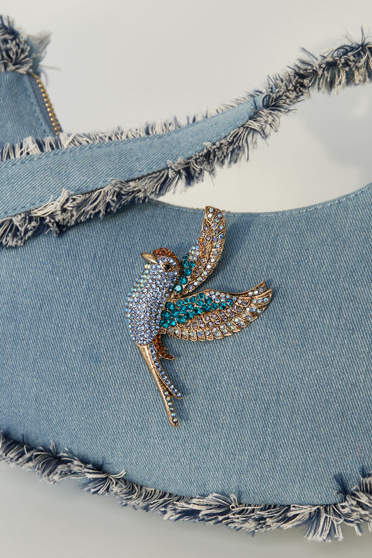 Blue rhinestone bird brooch pinned on light blue denim handbag with frayed edges