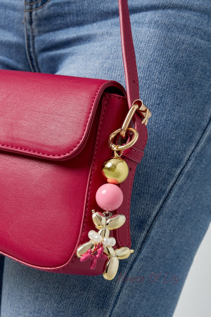 The gold and pink balloon dog bag charm attached to a vibrant pink purse, worn by a person in blue jeans