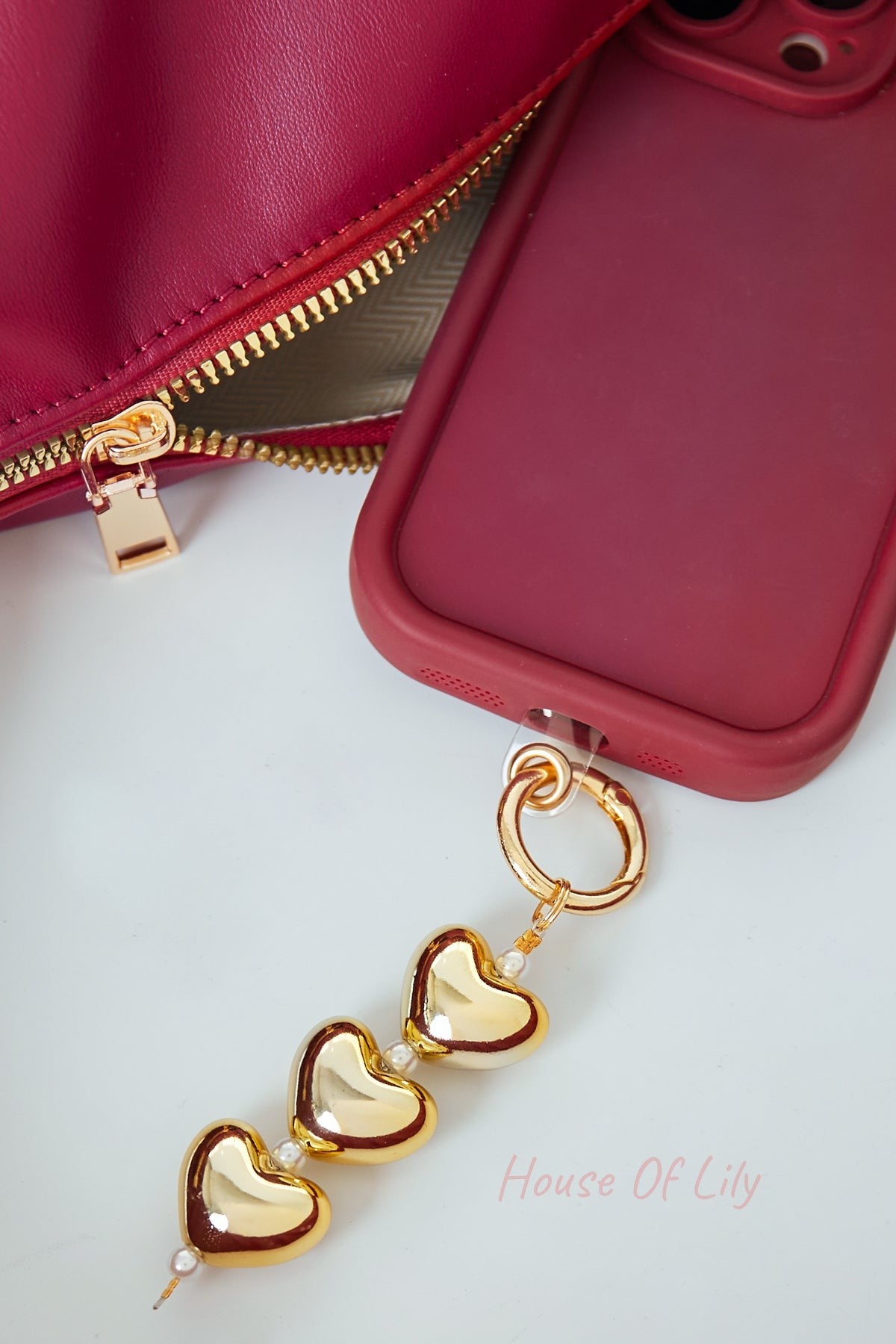 Gold heart and pearl charm attached to a phone case with matching red and gold accents