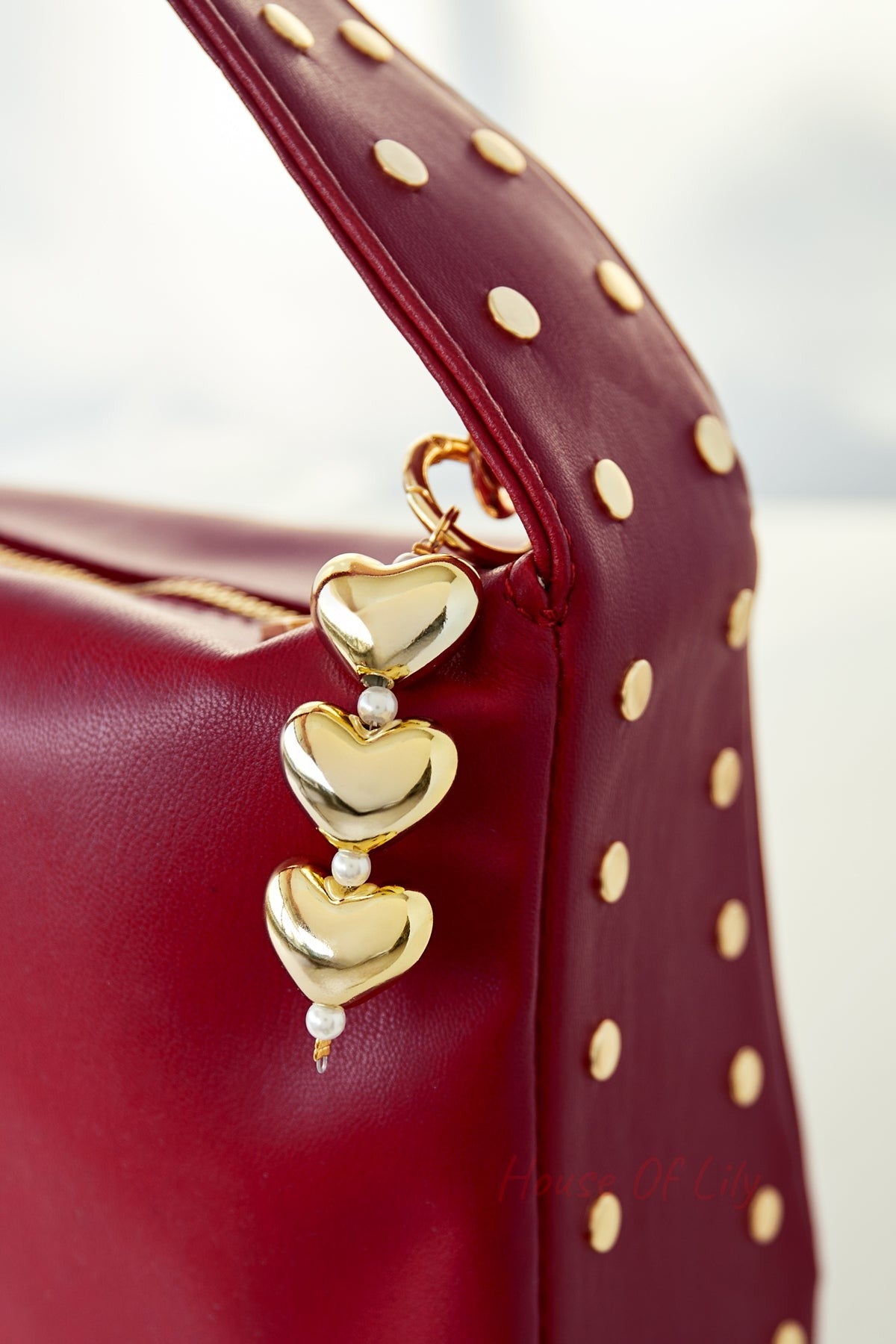 Close-up of gold heart and pearl charm hanging from a red studded handbag strap