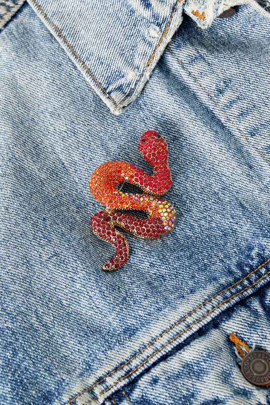 Red and orange crystal snake brooch pinned on blue denim jacket pocket