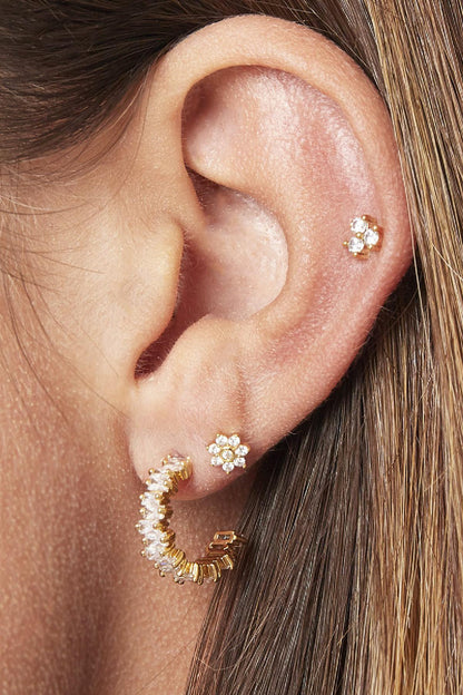 Close-up of a woman's ear wearing clear crystal baguette hoop earrings paired with small flower-shaped stud earrings