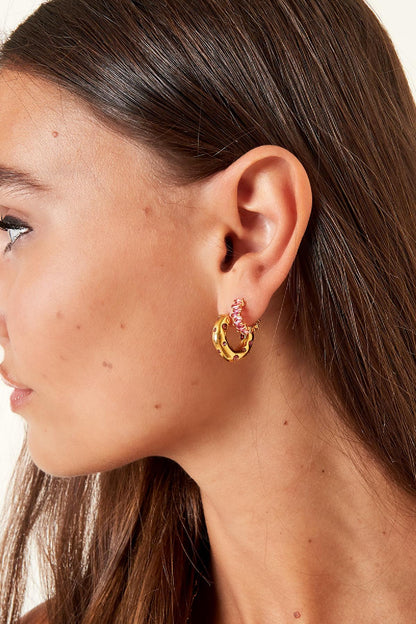 Side profile of a woman wearing pink crystal baguette hoop earrings stacked with gold textured hoop earrings