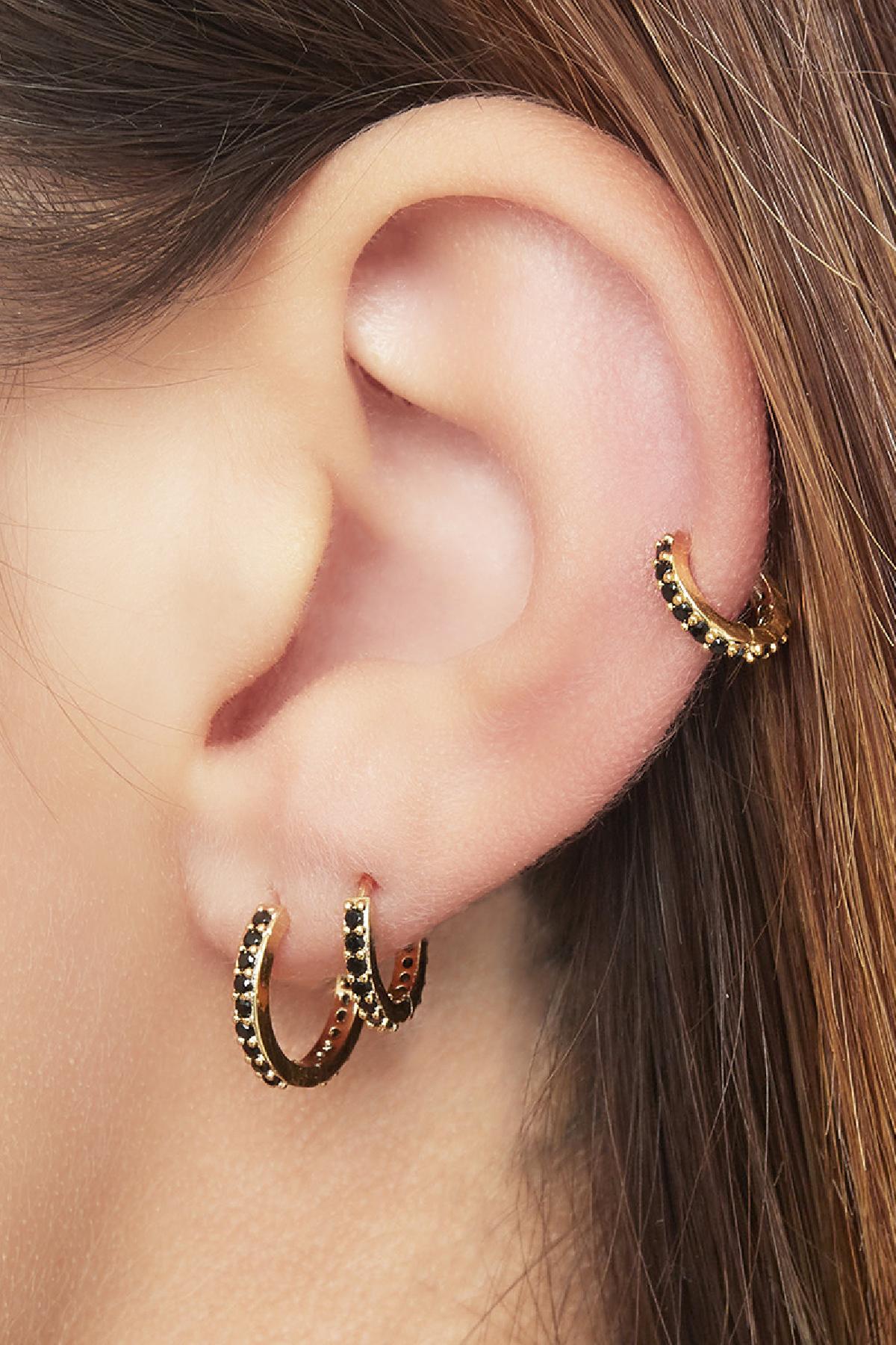Close-up of an ear wearing three gold-tone hoop earrings with black stones, showing stacked and layered look