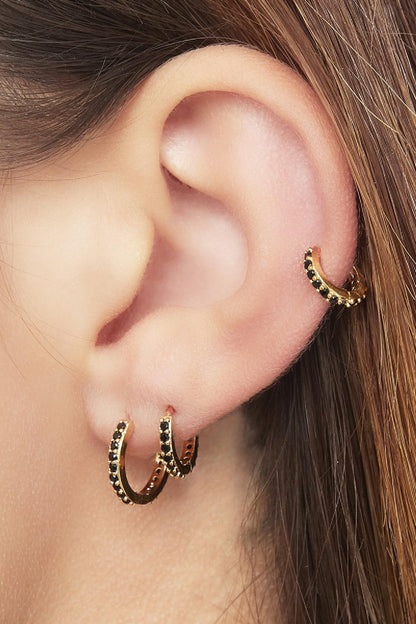 Close-up of an ear wearing three gold-tone hoop earrings with black stones, showing stacked and layered look