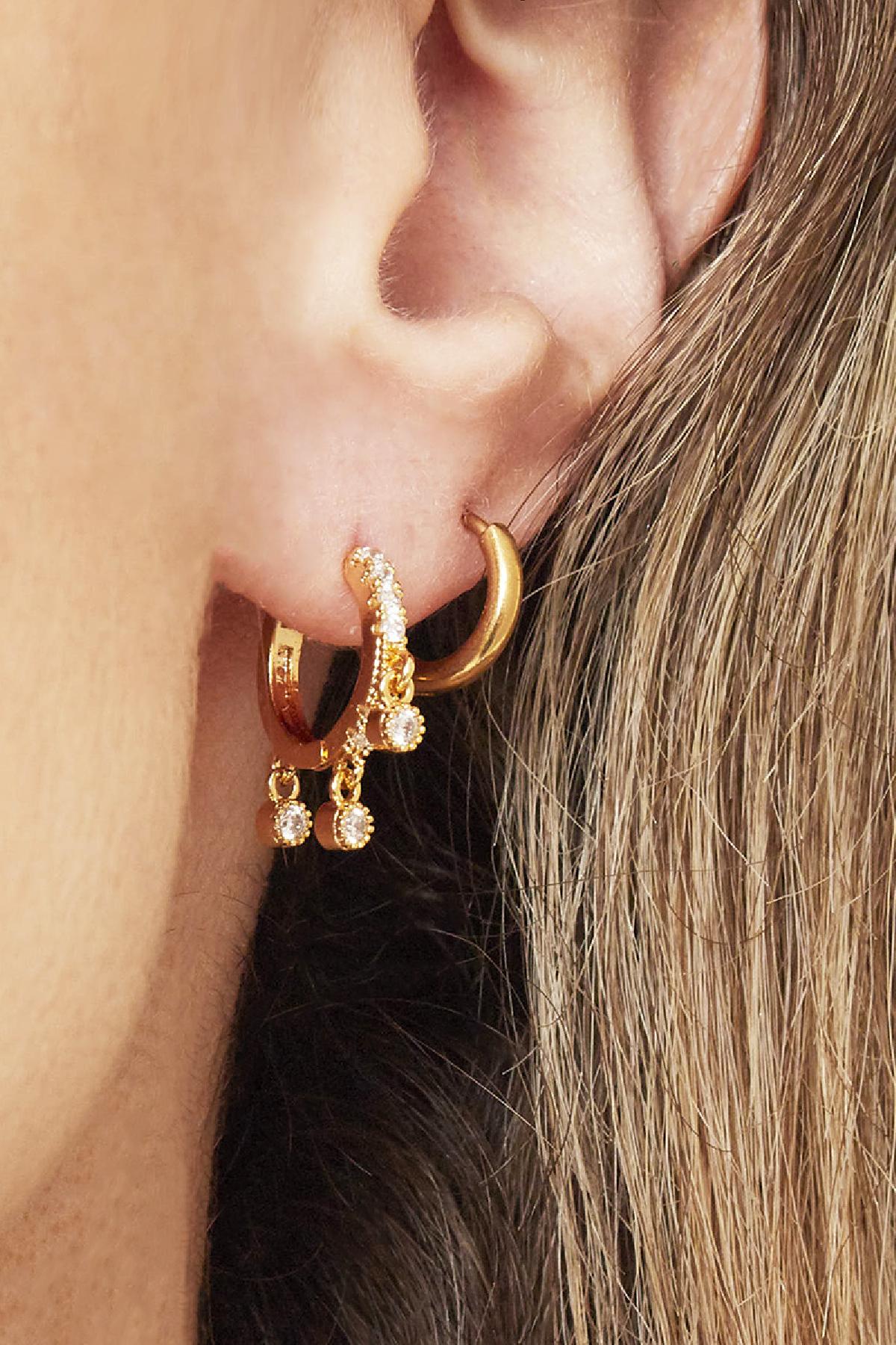 Close-up of ear wearing stacked gold hoop earrings, including one with small dangling charms