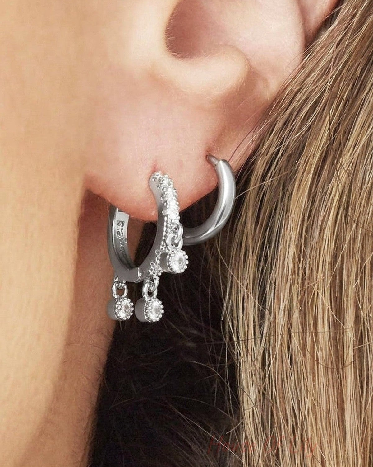 Silver hoop earrings with textured detailing and three dangling round crystal charms worn in ear piercings.