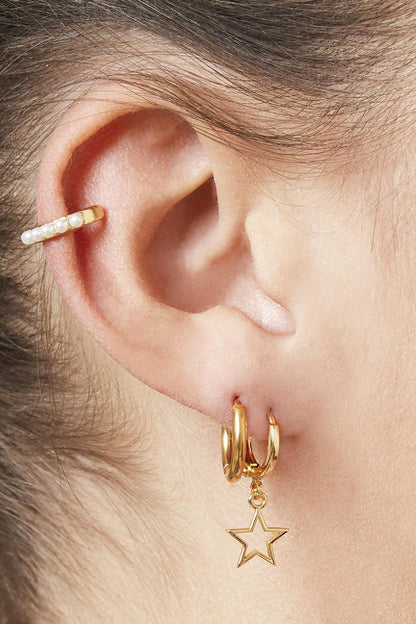 Close-up of woman's ear wearing layered gold hoops, one with a star charm and a pearl-studded ear cuff
