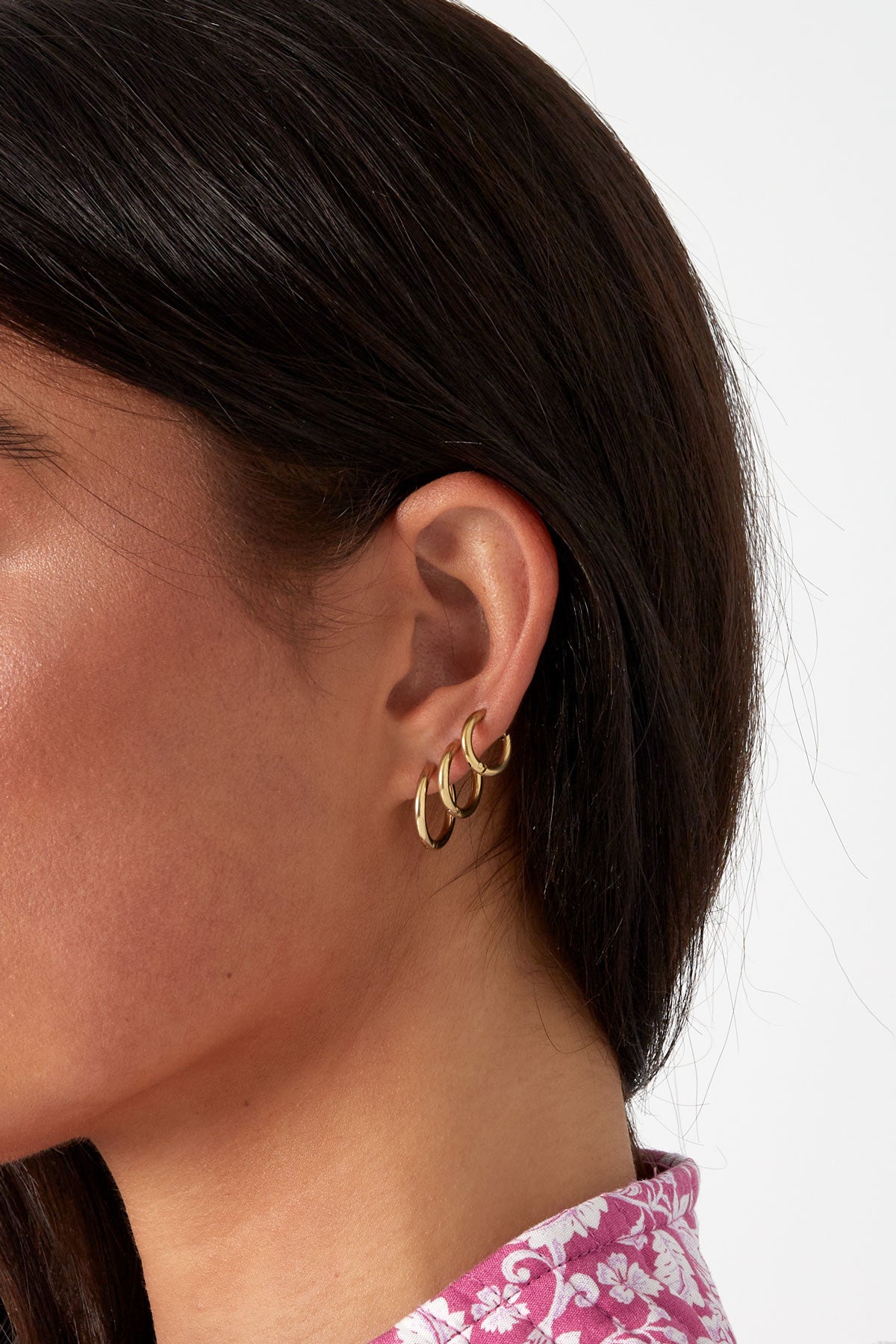 Close-up of a woman wearing three gold hoop earrings of varying sizes on her ear, showcasing a stylish layering look