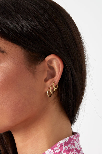 Close-up of a woman wearing three gold hoop earrings of varying sizes on her ear, showcasing a stylish layering look