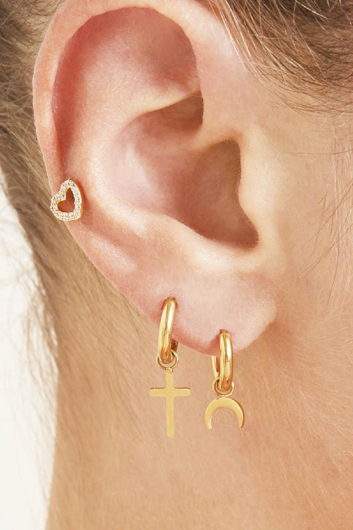 Side view of a woman's ear adorned with two gold hoop earrings with cross and crescent moon charms and a small heart stud earring
