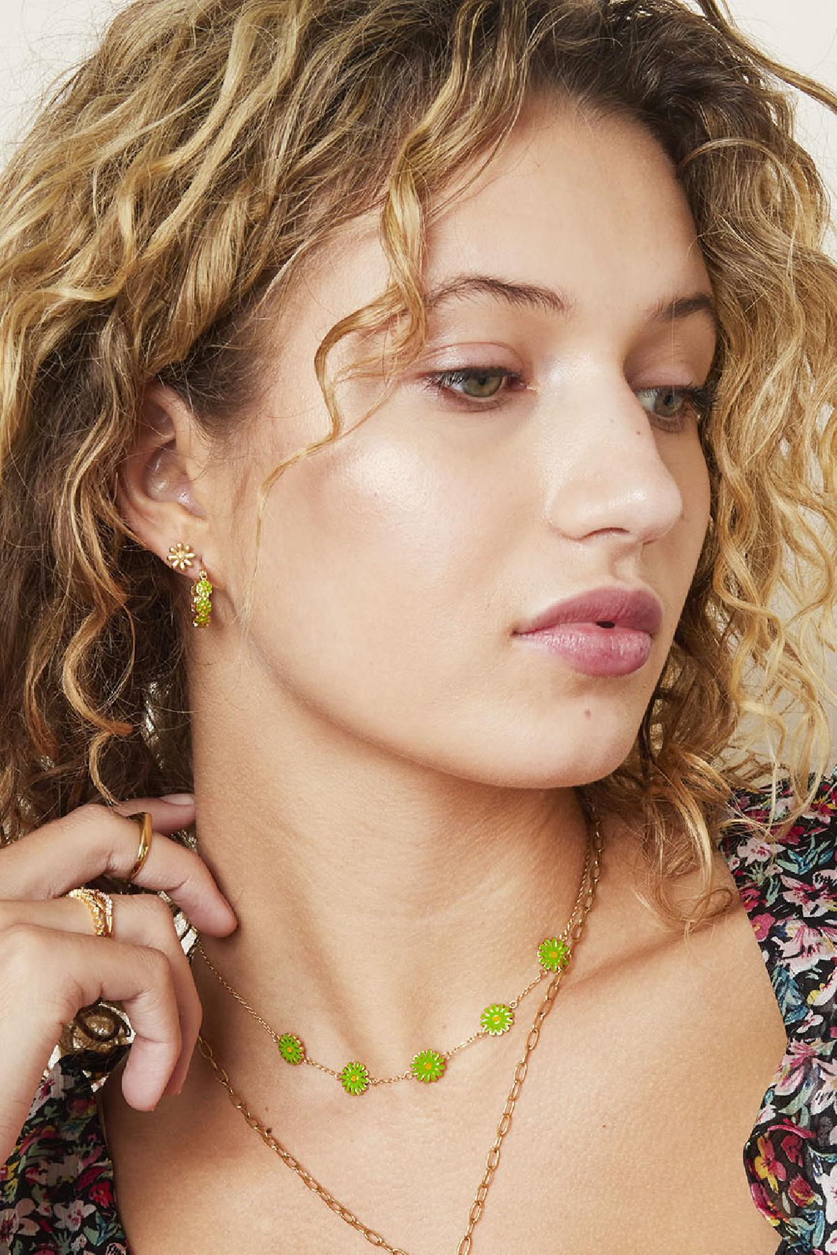 Model wearing gold daisy stud earrings with matching green floral necklace and hoop earrings