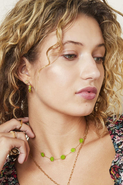 Model wearing gold daisy stud earrings with matching green floral necklace and hoop earrings