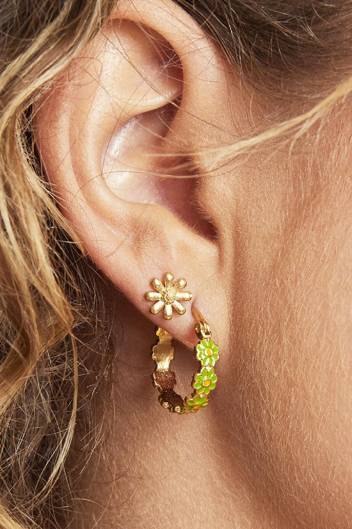 Close-up of ear wearing a gold daisy stud earring and green floral hoop earring
