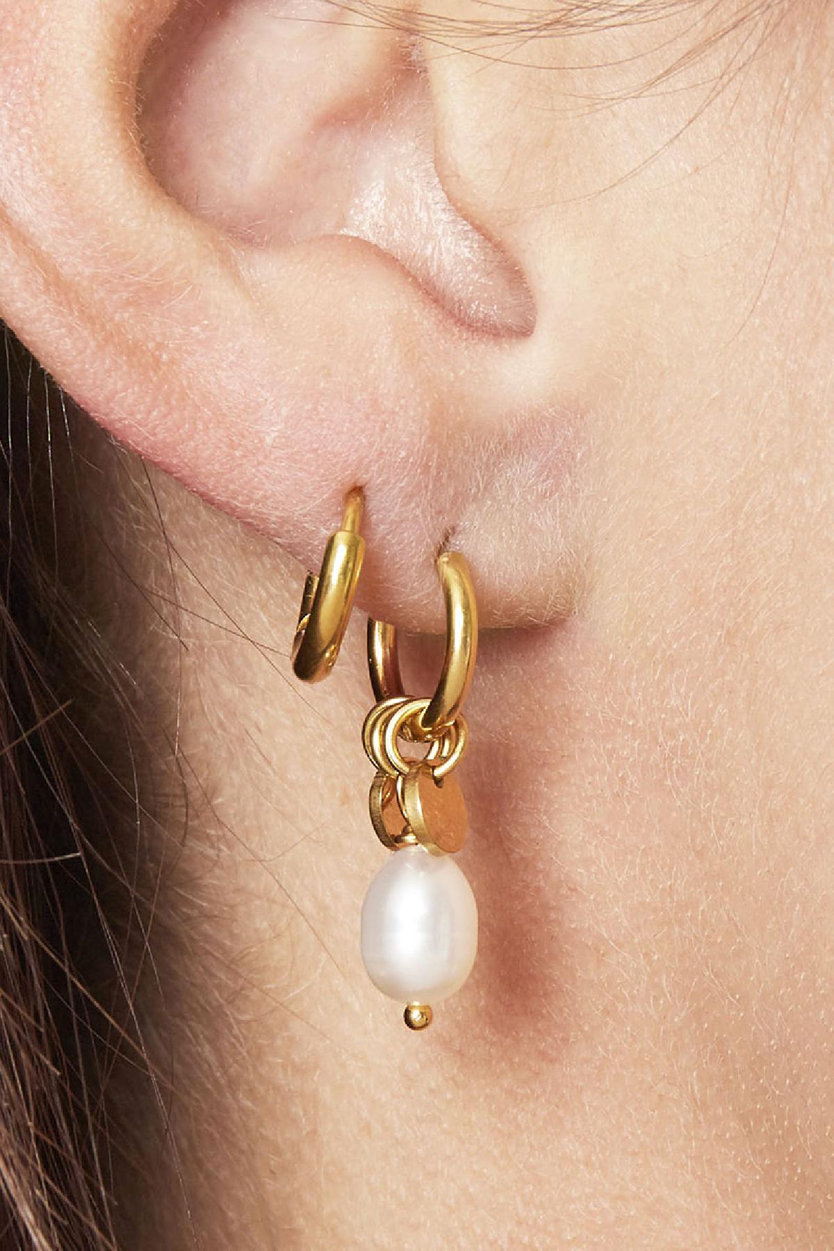 Close-up of a woman wearing gold hoop earrings with pearl drops and small disc charms on her ear