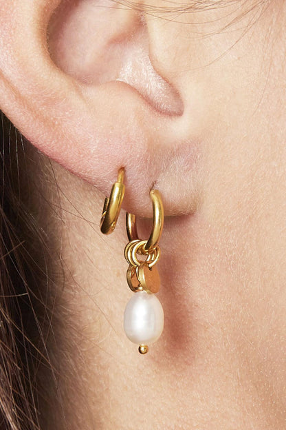 Close-up of a woman wearing gold hoop earrings with pearl drops and small disc charms on her ear