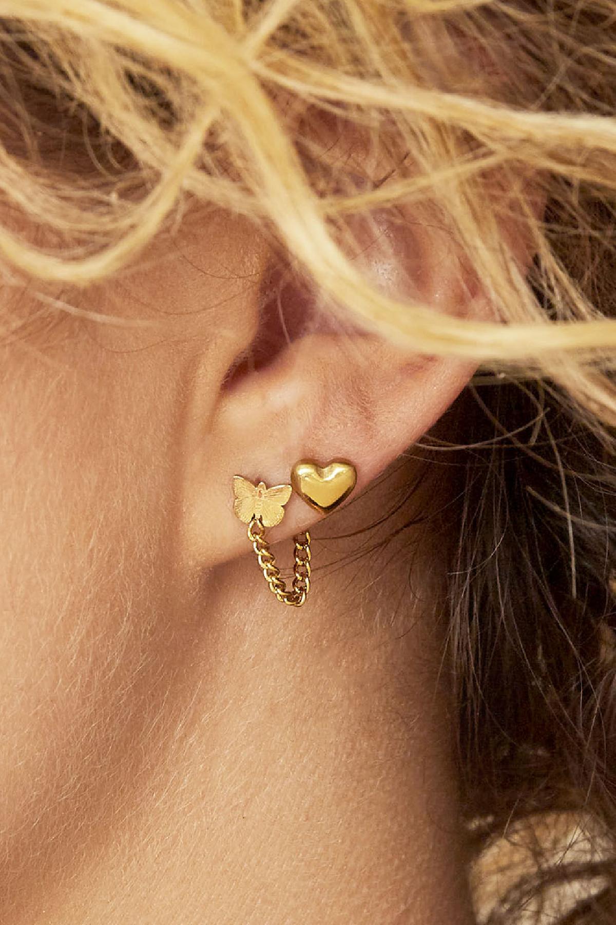 Close-up of ear with gold heart stud earring paired with a small butterfly earring connected by a gold chain