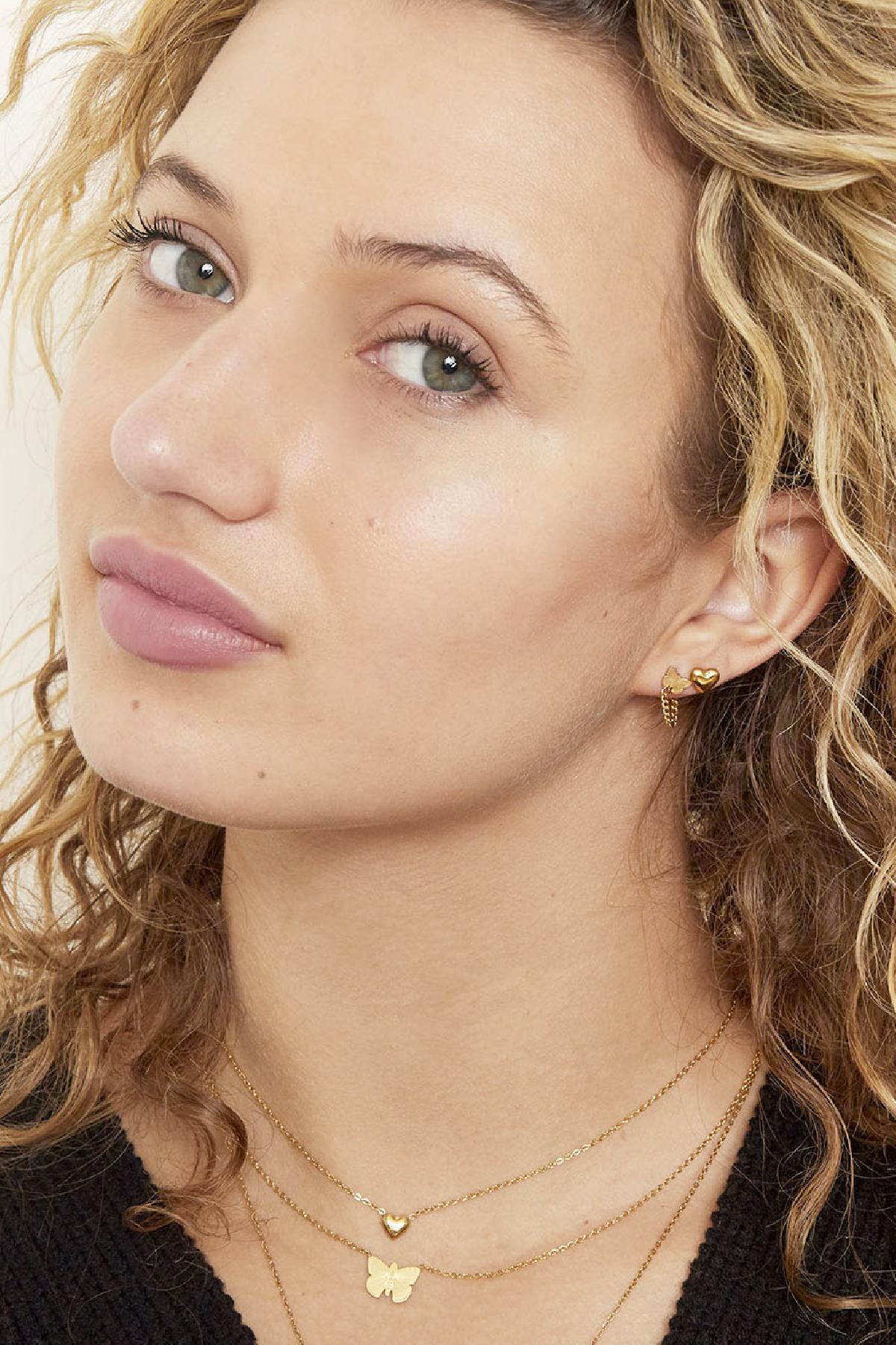 Model wearing gold heart stud earrings with layered gold necklaces featuring heart and butterfly pendants