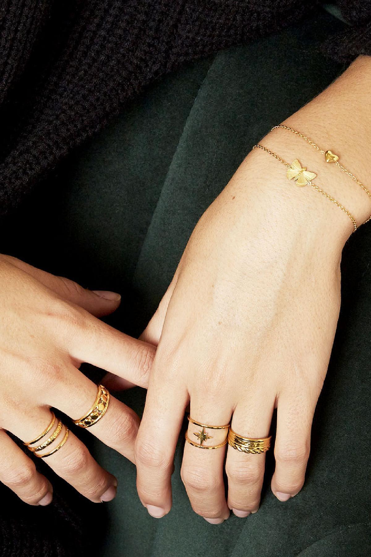 Model wrist adorned with slim gold bracelets featuring butterfly and heart charms, showcasing sporty youthful jewellery style