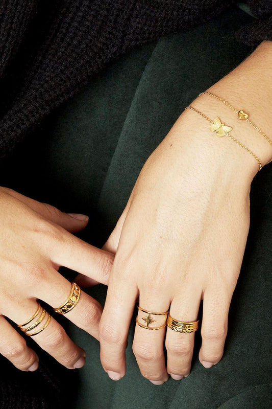 Model wrist adorned with slim gold bracelets featuring butterfly and heart charms, showcasing sporty youthful jewellery style