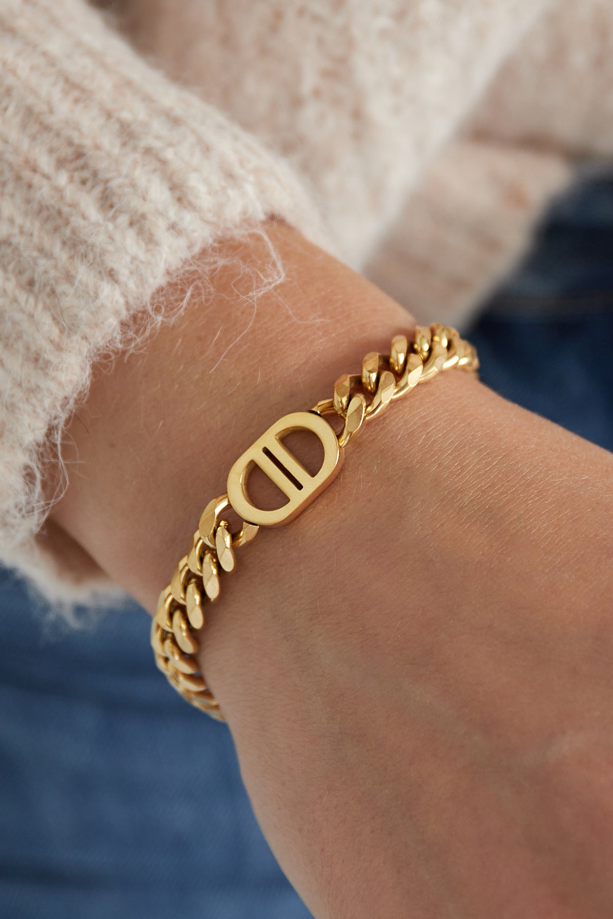 Gold chunky chain link bracelet on wrist with cream sweater and blue jeans showcasing the oval dual-bar centerpiece