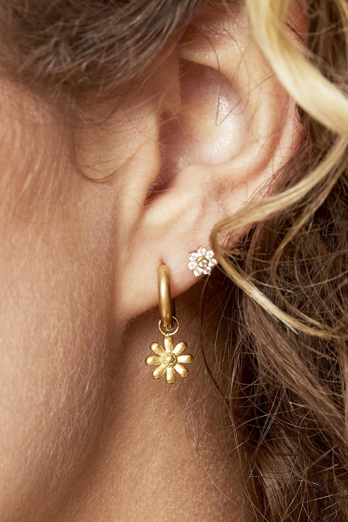 Close-up of woman's ear wearing gold daisy charm hoop earring paired with small rhinestone stud earring