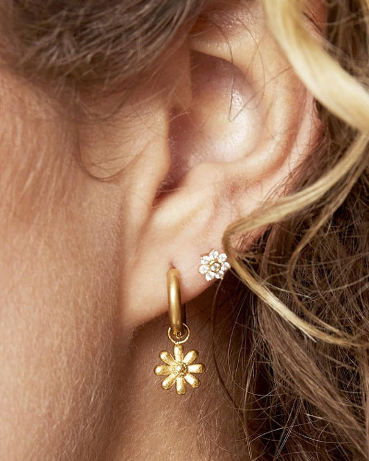Close-up of woman's ear wearing gold daisy charm hoop earring paired with small rhinestone stud earring