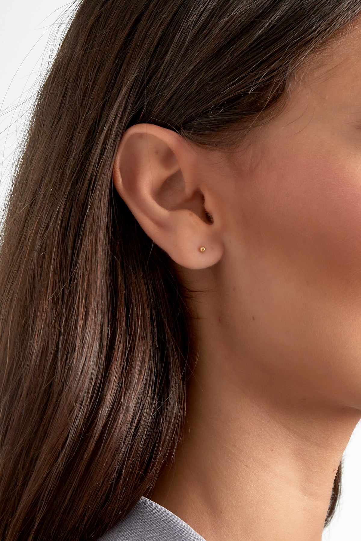 Close up of a woman wearing a small gold dot stud earring, showcasing its minimalist design