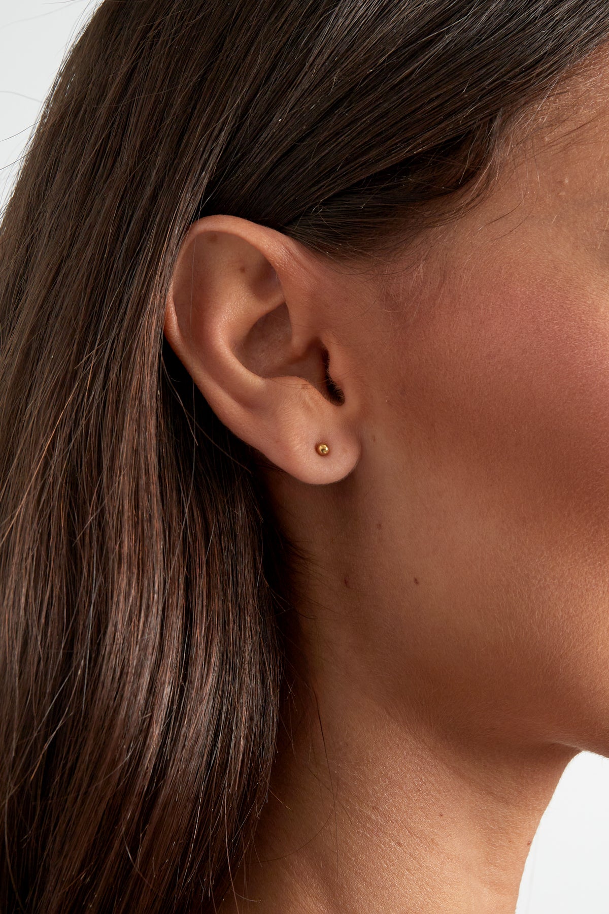 Close-up of a woman's ear wearing a single small gold ball stud earring showcasing minimalist style