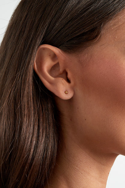 Close-up of a woman's ear wearing a single small gold ball stud earring showcasing minimalist style