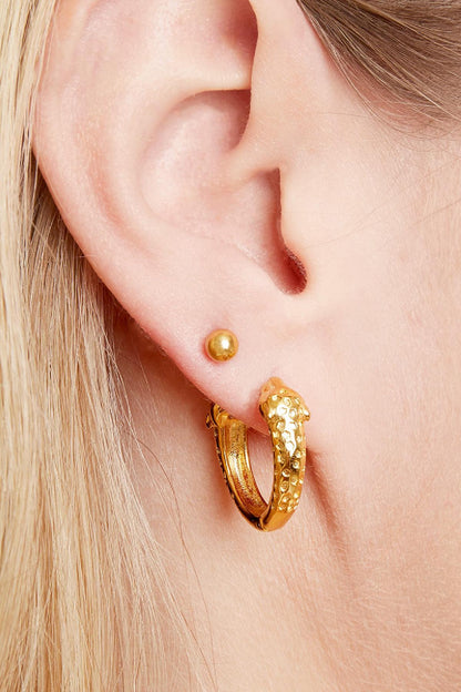 Close-up of an ear wearing a small gold ball stud earring above a gold textured hoop earring