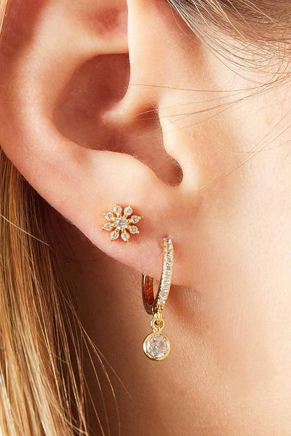Side view of a woman's ear wearing a gold-tone crystal flower piercing earring paired with a small crystal hoop earring