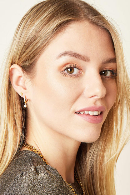 Portrait of a smiling woman with blonde hair wearing the gold crystal flower piercing earring alongside a stylish gold chain necklace