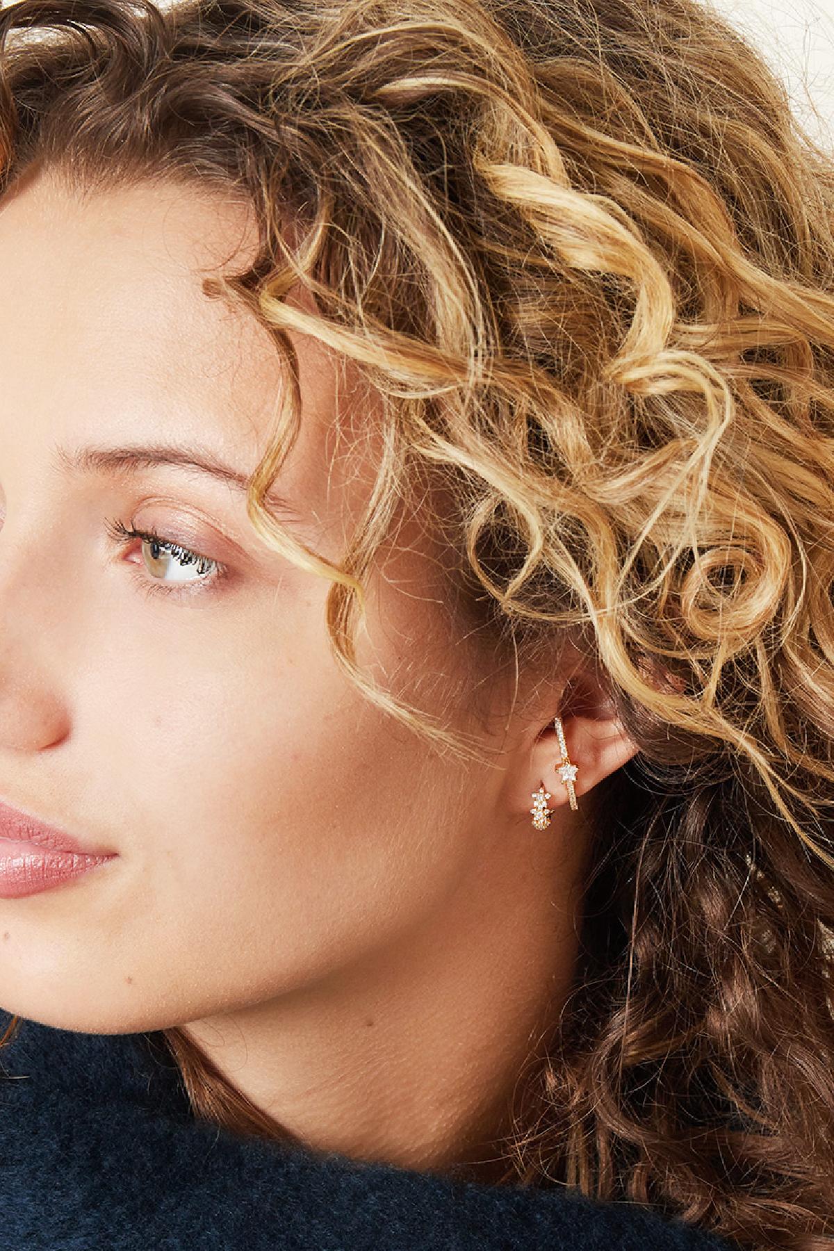 Side profile of woman wearing paired star design earrings in gold with rhinestones