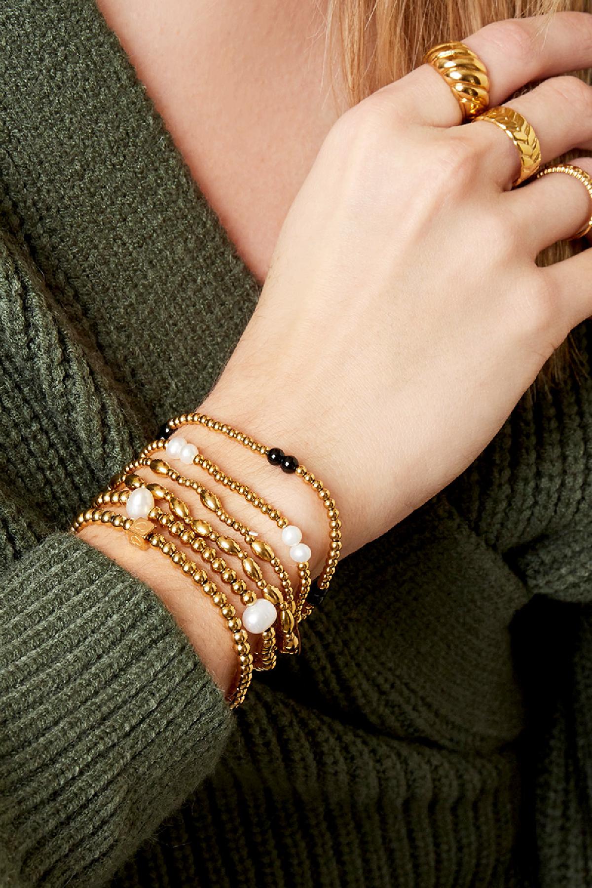 Close-up of wrist wearing multiple gold and pearl beaded bracelets paired with gold rings and a green sweater