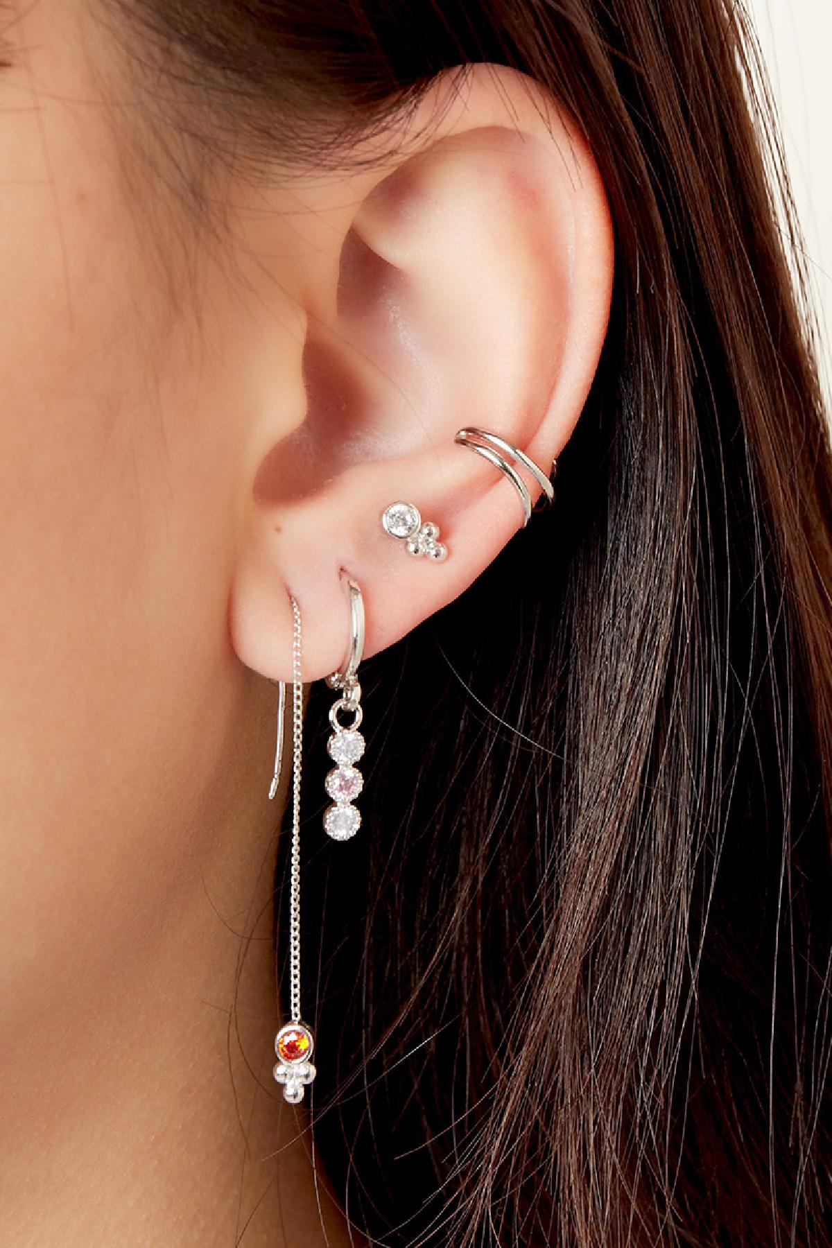 Close-up photo of an ear wearing silver earrings including a silver spiral ear cuff, dangling earrings with crystals, and small studs, showcasing elegant ear styling.