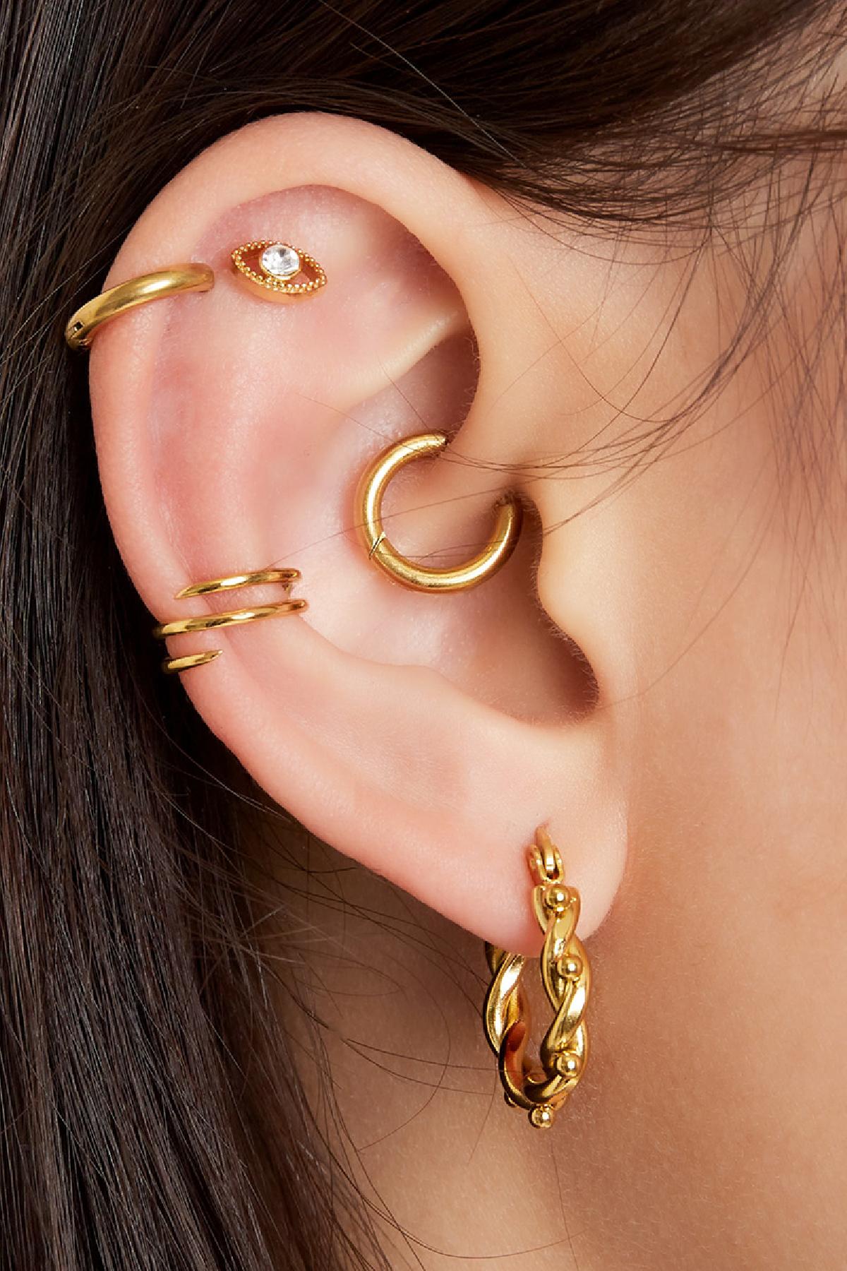 Photo showing an ear adorned with multiple gold earrings including a spiral ear cuff, hoop, and studs, highlighting layered jewelry styling.