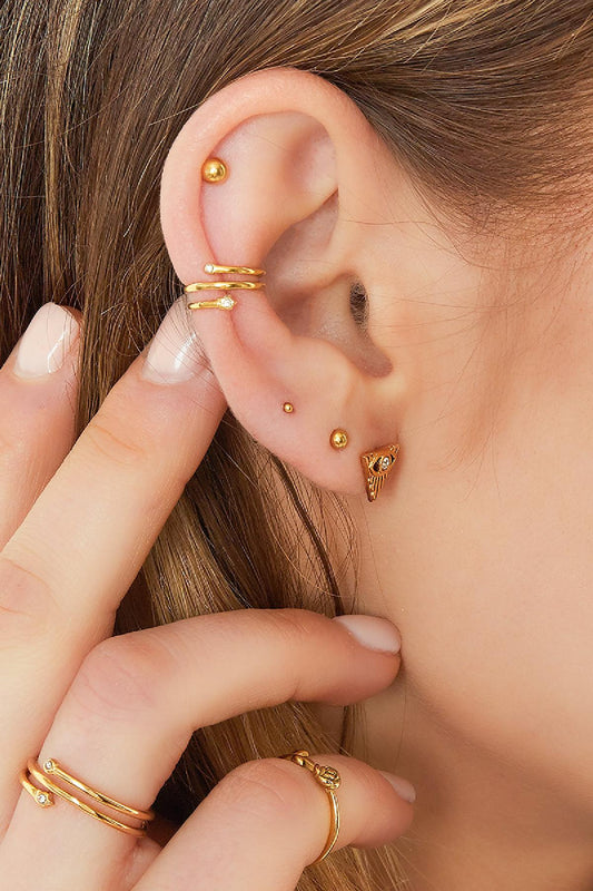 Close-up model ear wearing a gold spiral earcuff with zircon stones and matching gold earrings and rings